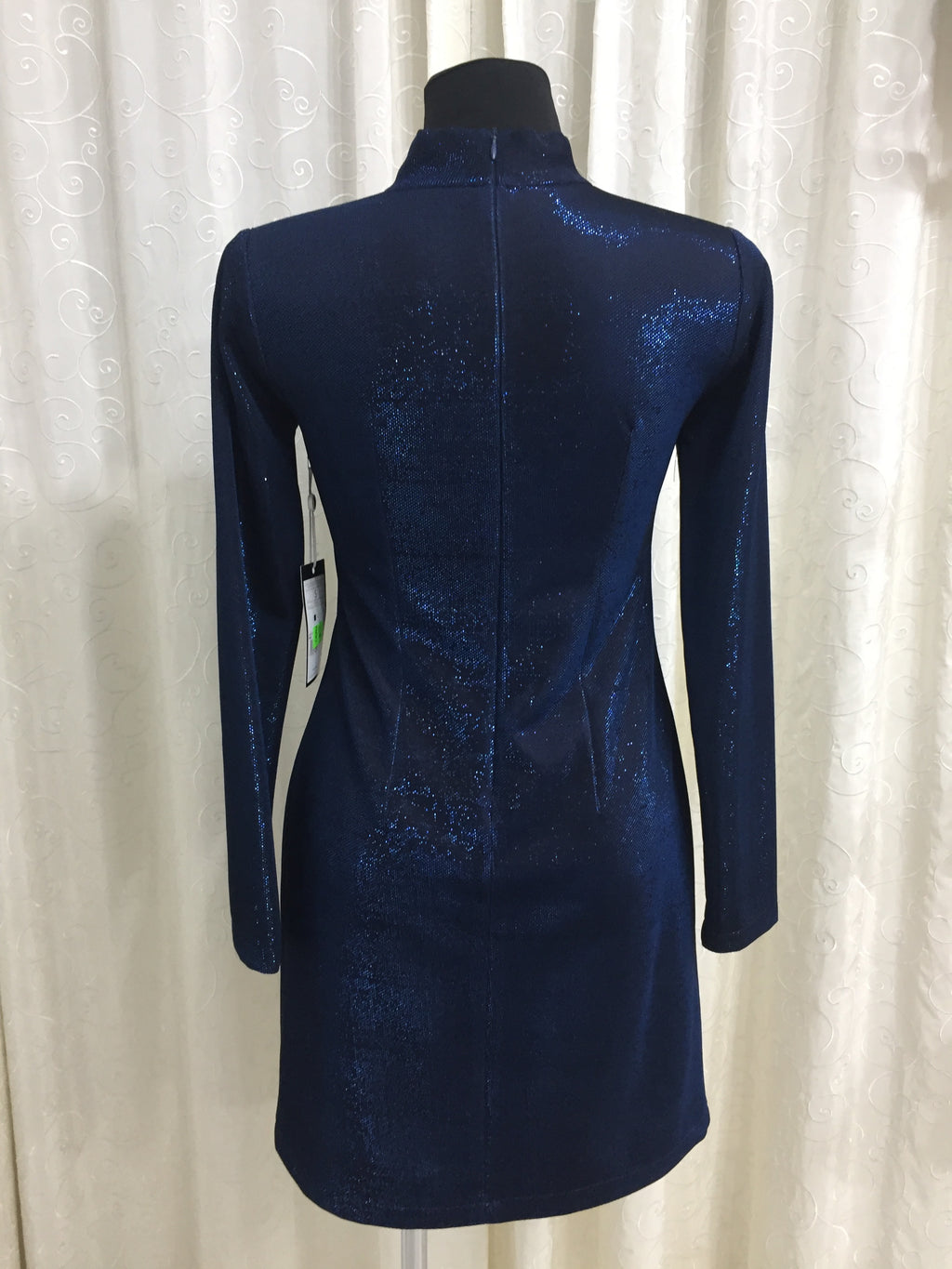 Metalické modré mini priliehavé šaty s dlhým rukávom a výstrihom a stojačikom okolo krku. Zapínanie na zips na zadnom diely. Zloženie: Polyester 95% Elastan 5%